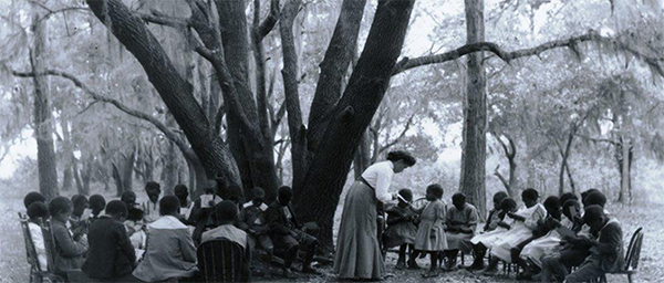 Early teachers at the Penn Center education a group of school-age children under the school ground's ancient oaks.