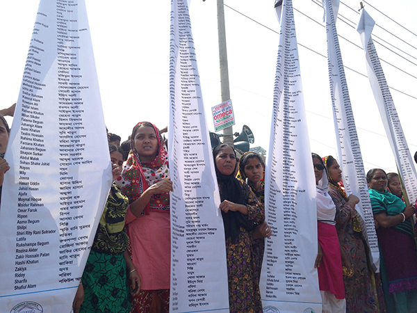 On the first anniversary of the Rana Plaza building collapse, family members and friends hold banners displaying the names of victims who were killed in the disaster. Credit: Worker Rights Consortium